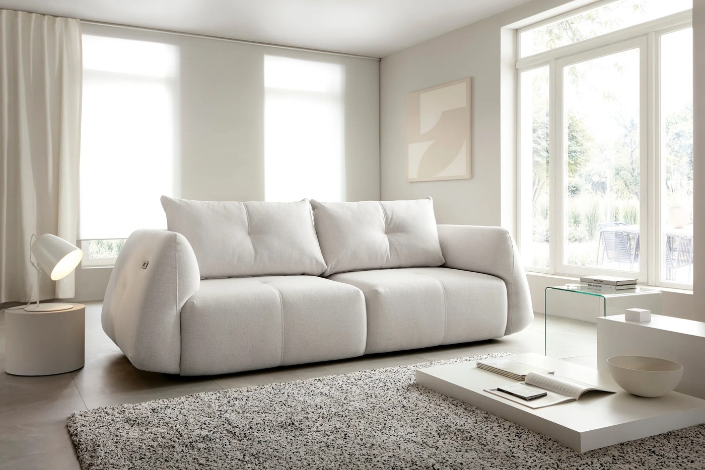 Pohovka RELAXIA sofa v svetlom čalúnení v interiéri pri veľkých oknách.