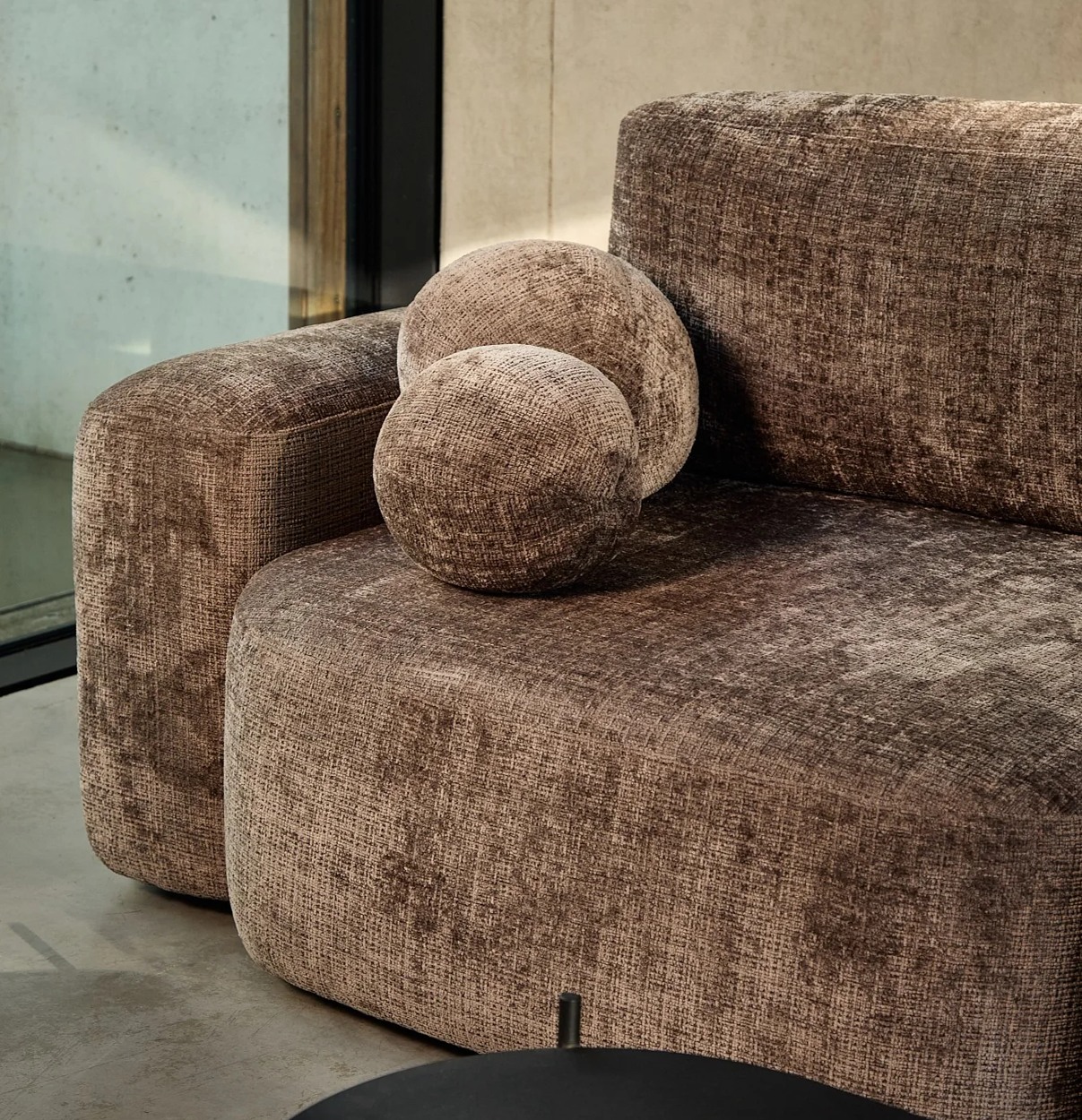 Detail sedu, oblých podrúčok a okrúhlych vankúšov VANESSA sofa v sivohnedom poťahu.