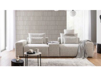 Pohovka LUNA SOFA 2 (1,5BL + PANEL + 1,5BP) v svetlom krémovom prevedení v obývačke, pohľad spredu so stolíkom, lampou a dekou.